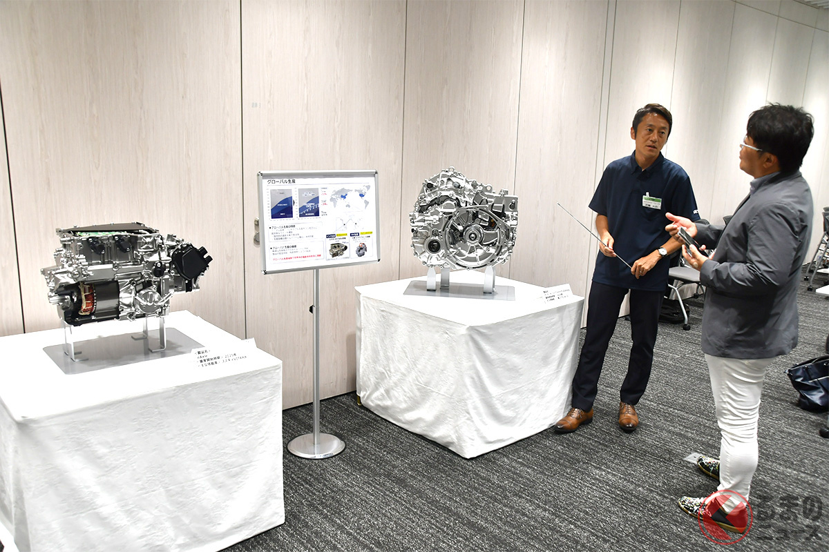 スズキeビターラ用eAxleと三菱エクスフォース用ハイブリッドミッションを前に取材する筆者(山本シンヤ)